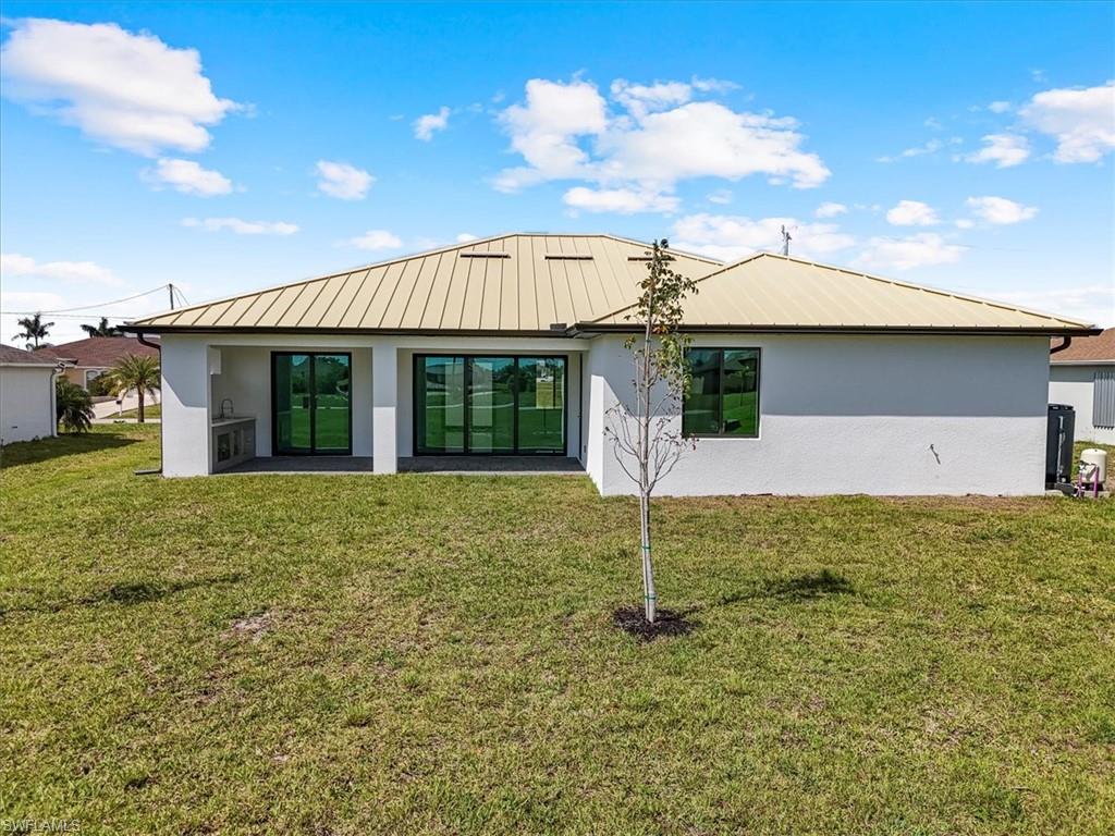 Back of house featuring stucco siding, metal roof, and a yard