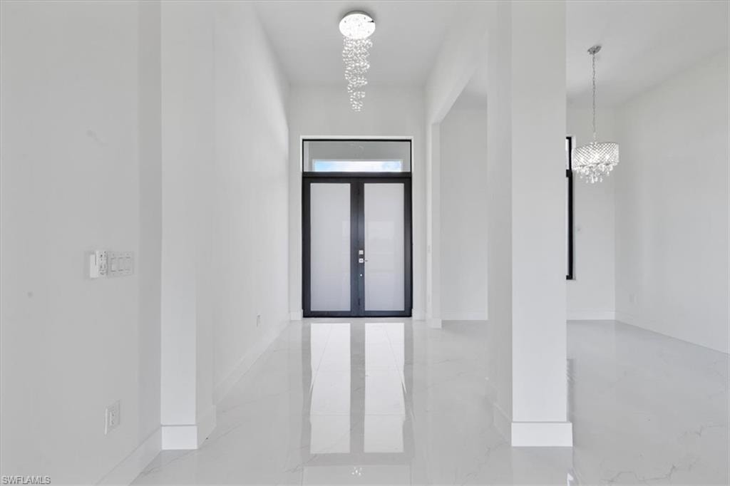 Corridor featuring an inviting chandelier, marble finish floor, and baseboards