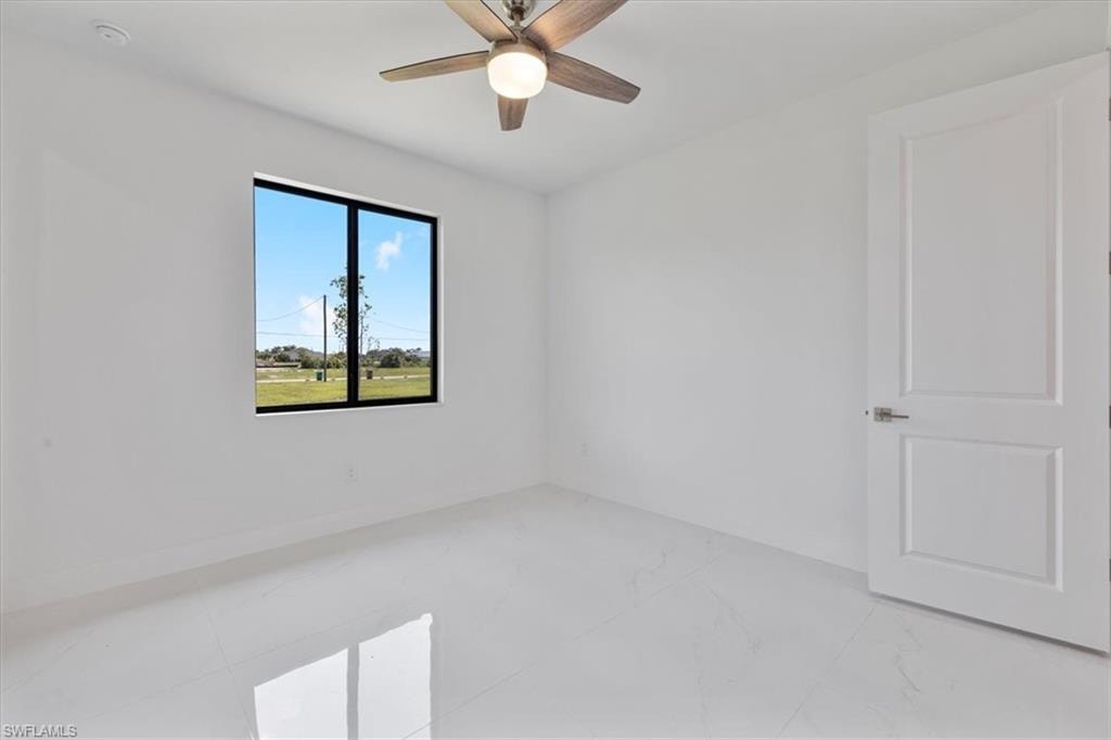 Empty room featuring marble finish floor, baseboards, and ceiling fan