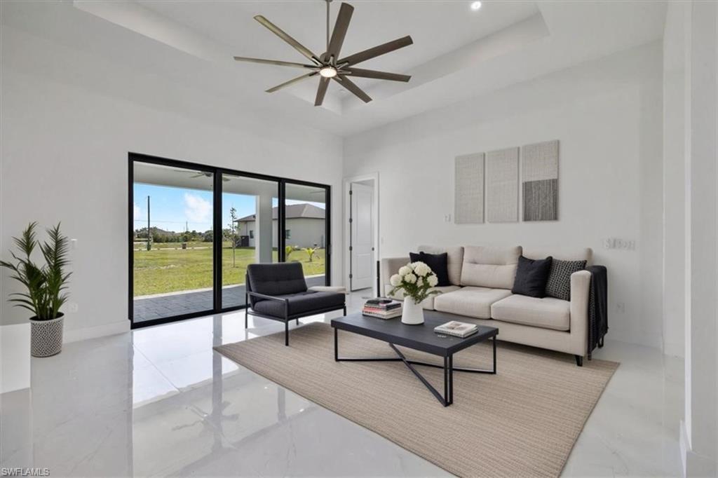 Living room with marble finish floor, a tray ceiling, a high ceiling, and a ceiling fan