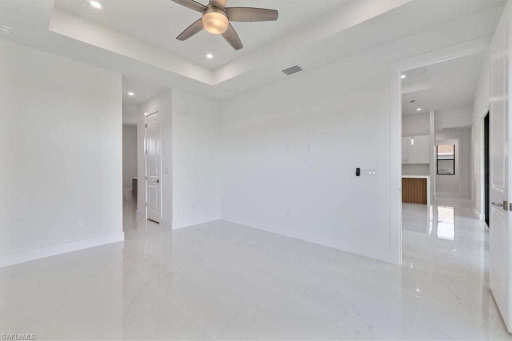 Spare room with marble finish floor, a raised ceiling, ceiling fan, and visible vents