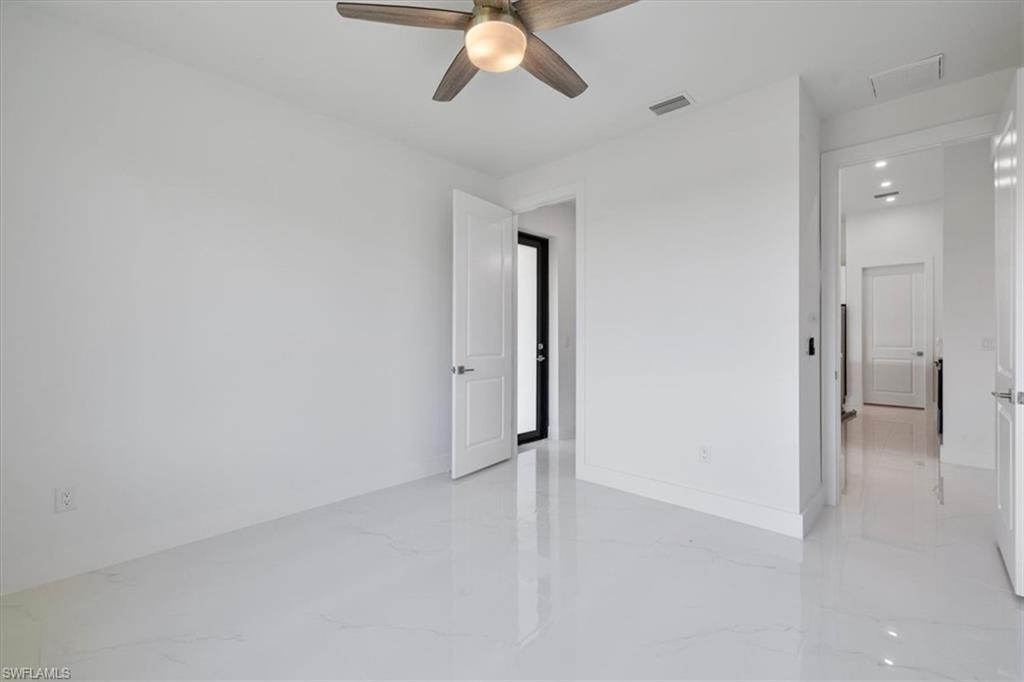Empty room with baseboards, marble finish floor, visible vents, and a ceiling fan