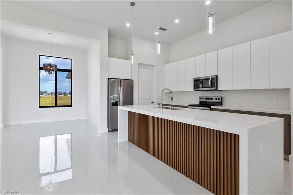Kitchen with light countertops, a sink, modern cabinets, stainless steel appliances, and a kitchen island with sink