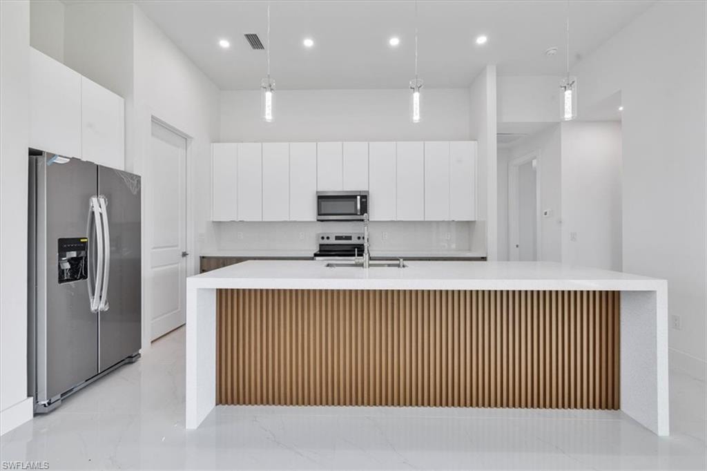 Kitchen featuring light countertops, visible vents, stainless steel appliances, tasteful backsplash, and white cabinetry