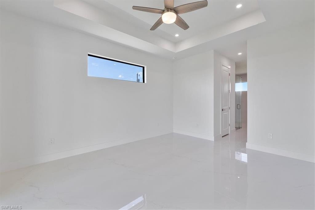 Unfurnished room with a tray ceiling, recessed lighting, baseboards, marble finish floor, and a ceiling fan