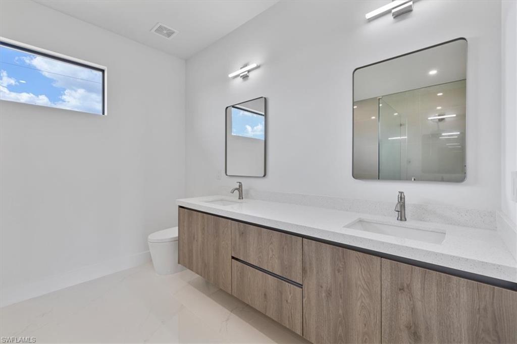 Full bathroom with toilet, a sink, double vanity, and visible vents