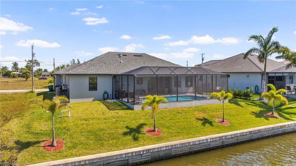 Rear view of house featuring stucco siding, a lawn, a water view, glass enclosure, and an outdoor pool