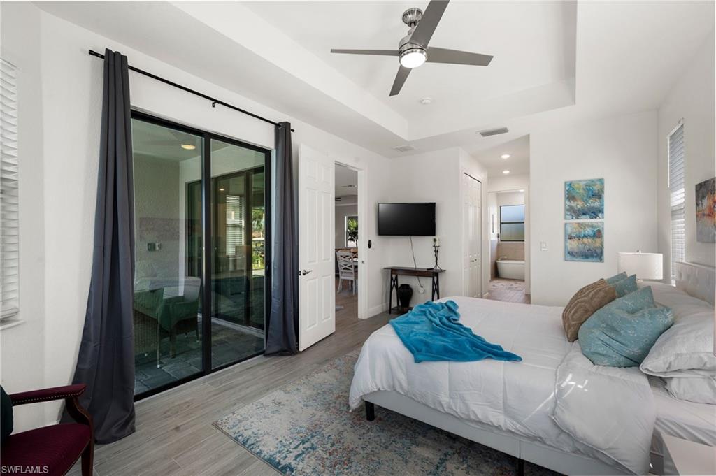 Bedroom with ensuite bath, visible vents, access to exterior, a raised ceiling, and wood finished floors