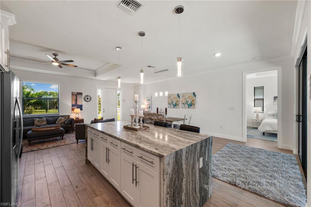 Kitchen with a tray ceiling, ornamental molding, visible vents, stainless steel fridge, and open floor plan