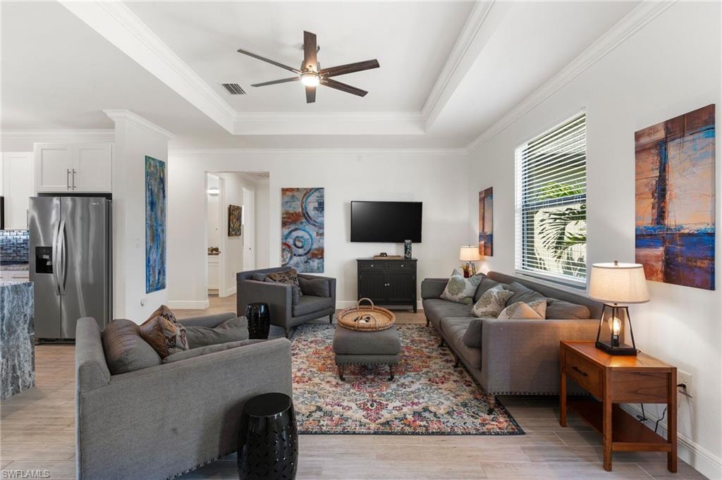 Living room featuring ornamental molding, light wood-style flooring, visible vents, a tray ceiling, and ceiling fan