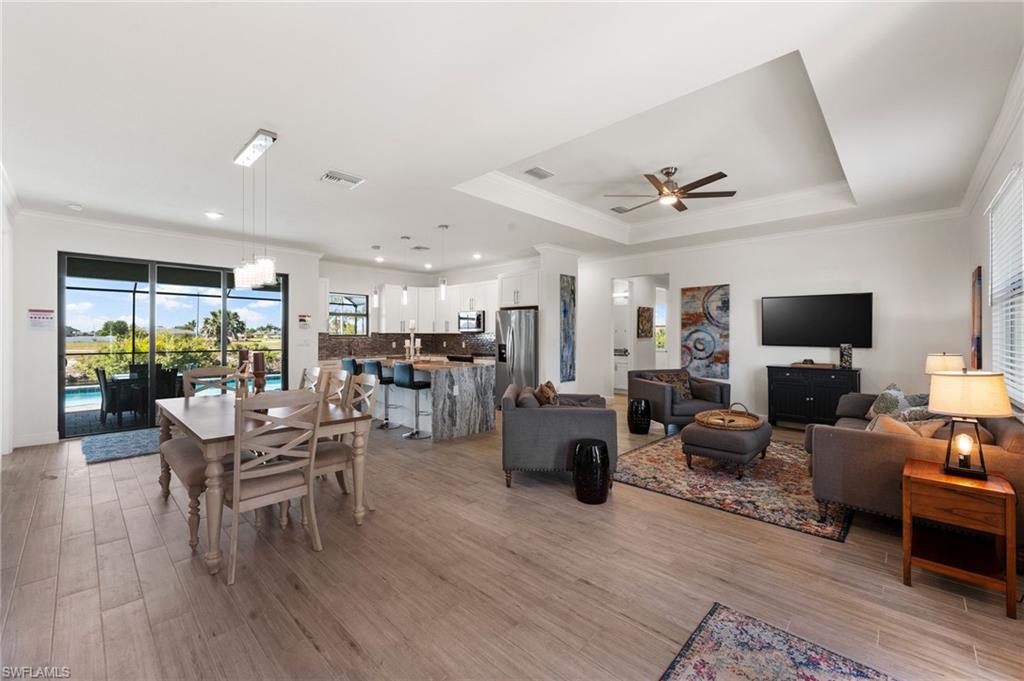 Dining area with a tray ceiling, light wood-type flooring, ornamental molding, a ceiling fan, and visible vents