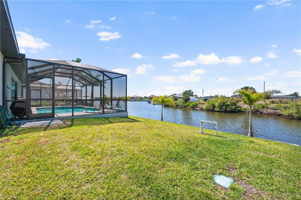 View of yard featuring a water view, an outdoor pool, and glass enclosure