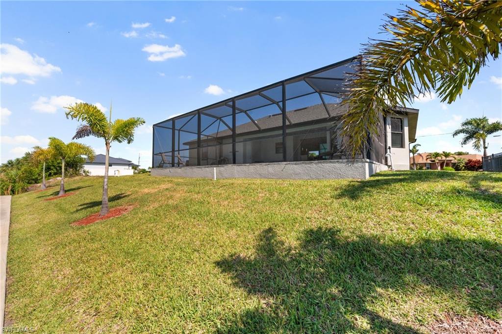 Back of house with a yard, stucco siding, and a lanai