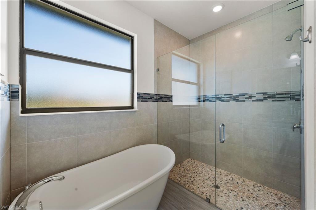 Bathroom featuring tile walls, a shower stall, and a soaking tub