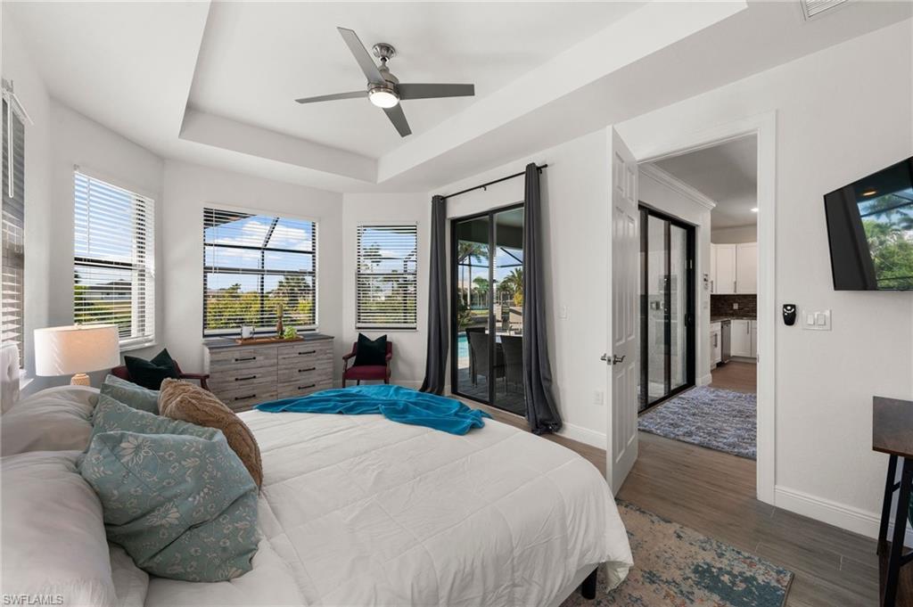 Bedroom featuring baseboards, ceiling fan, a tray ceiling, wood finished floors, and access to outside