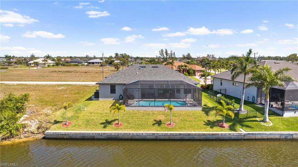 Back of property featuring a water view, a lanai, and a lawn