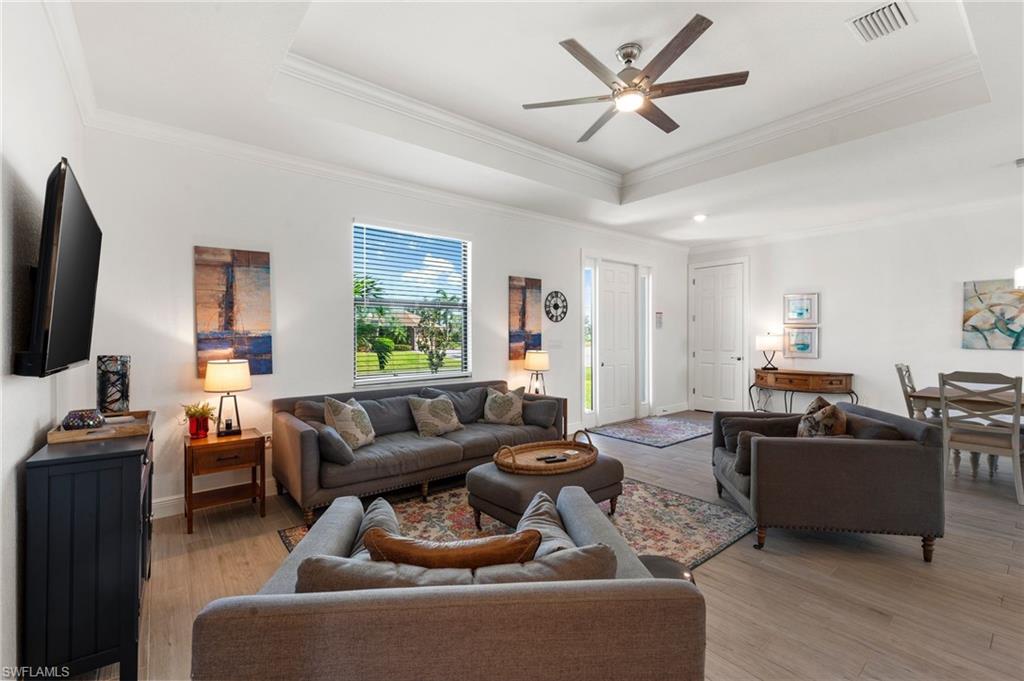 Living area featuring a tray ceiling, light wood-type flooring, and visible vents