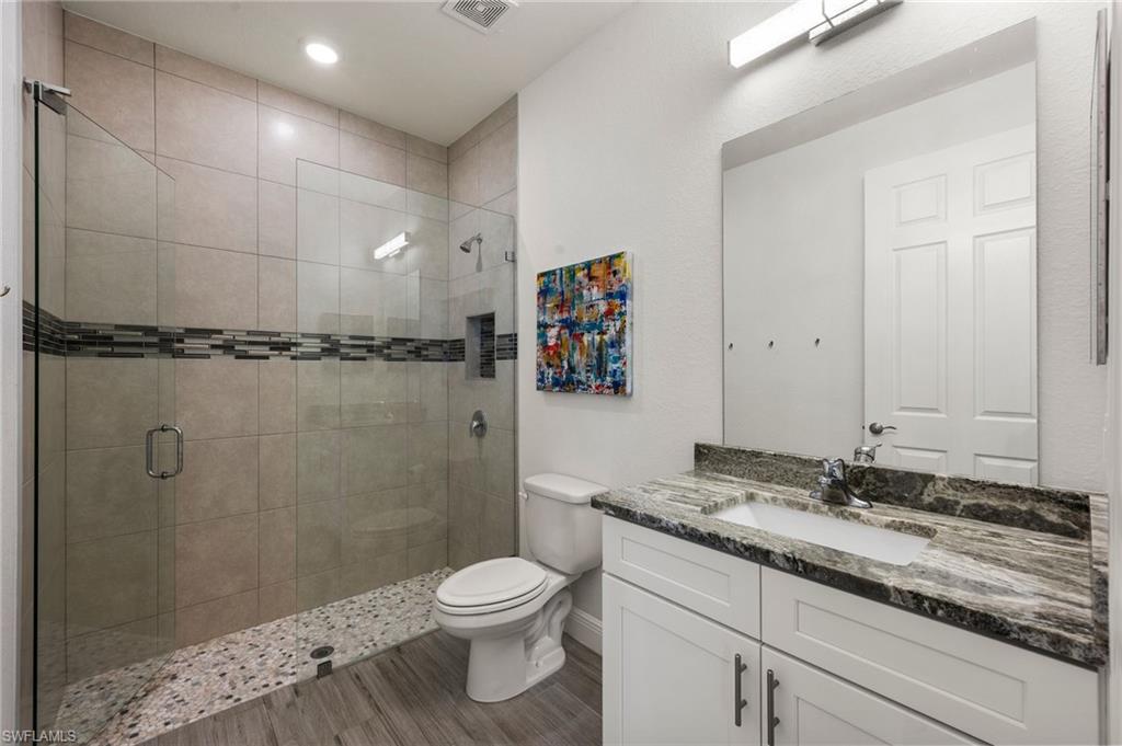 Bathroom with visible vents, toilet, a shower stall, vanity, and wood finished floors