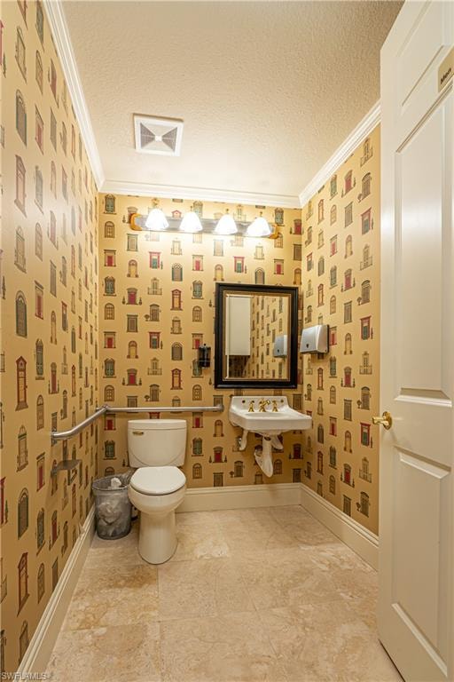 Bathroom with toilet, a textured ceiling, crown molding, and baseboards
