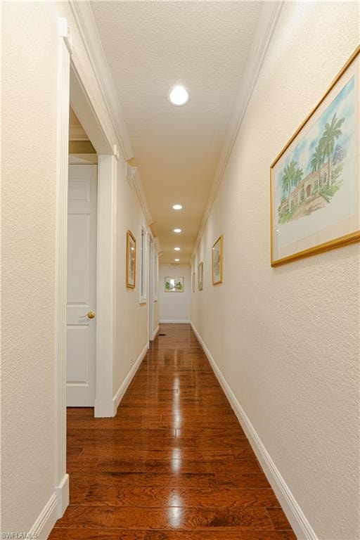 Hall featuring dark wood-style flooring, baseboards, a textured wall, recessed lighting, and crown molding