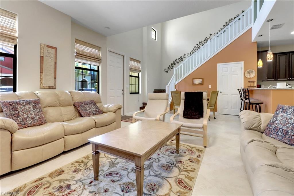 Living room with a high ceiling, light tile patterned flooring, visible vents, and stairs