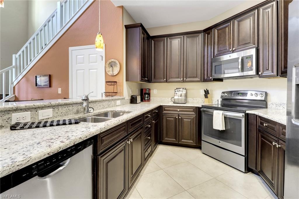 Kitchen featuring a sink, light tile patterned floors, appliances with stainless steel finishes, and dark brown cabinetry