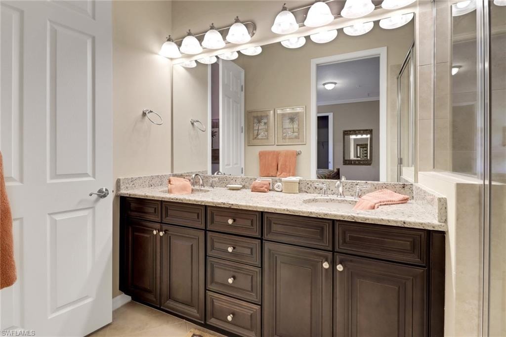 Ensuite bathroom featuring a sink, crown molding, double vanity, connected bathroom, and a shower with door