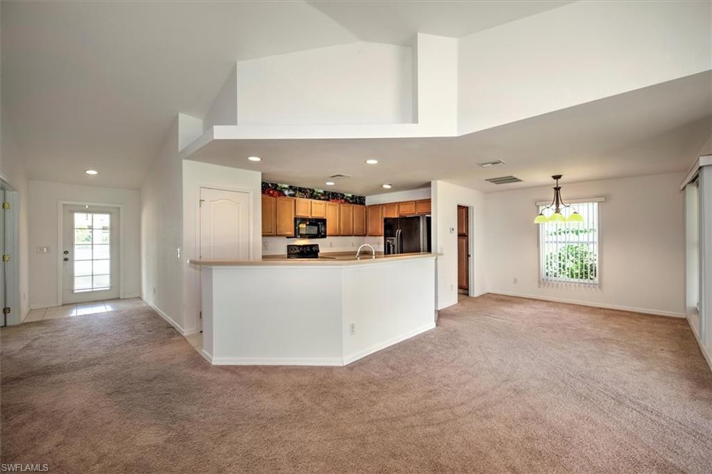 Kitchen with black appliances, decorative light fixtures, a towering ceiling, a notable chandelier, and light colored carpet