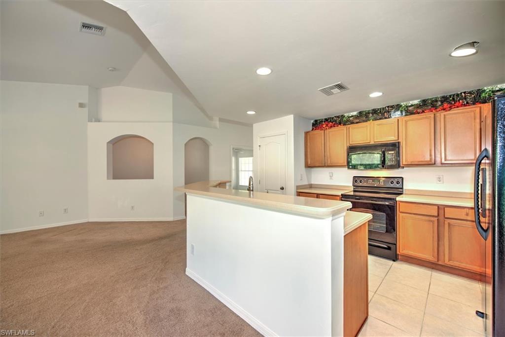Kitchen with light tile, black appliances, vaulted ceiling, and an island with sink
