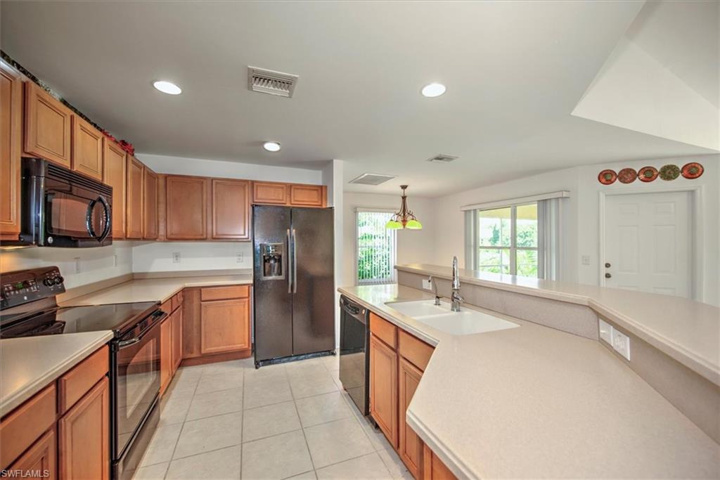 Kitchen with black appliances, sink, light tile floors, and pendant lighting