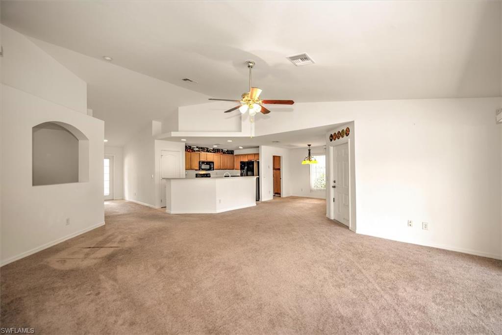 Great room room featuring light colored carpet, high vaulted ceiling, and ceiling fan