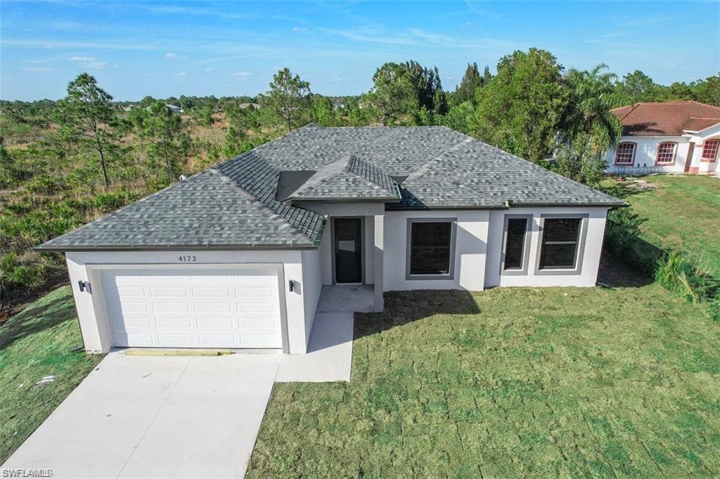 Single story home with a shingled roof, stucco siding, an attached garage, a front lawn, and driveway