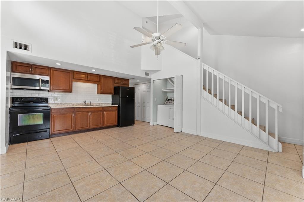 Kitchen with high vaulted ceiling, visible vents, black appliances, washing machine and clothes dryer, and light countertops