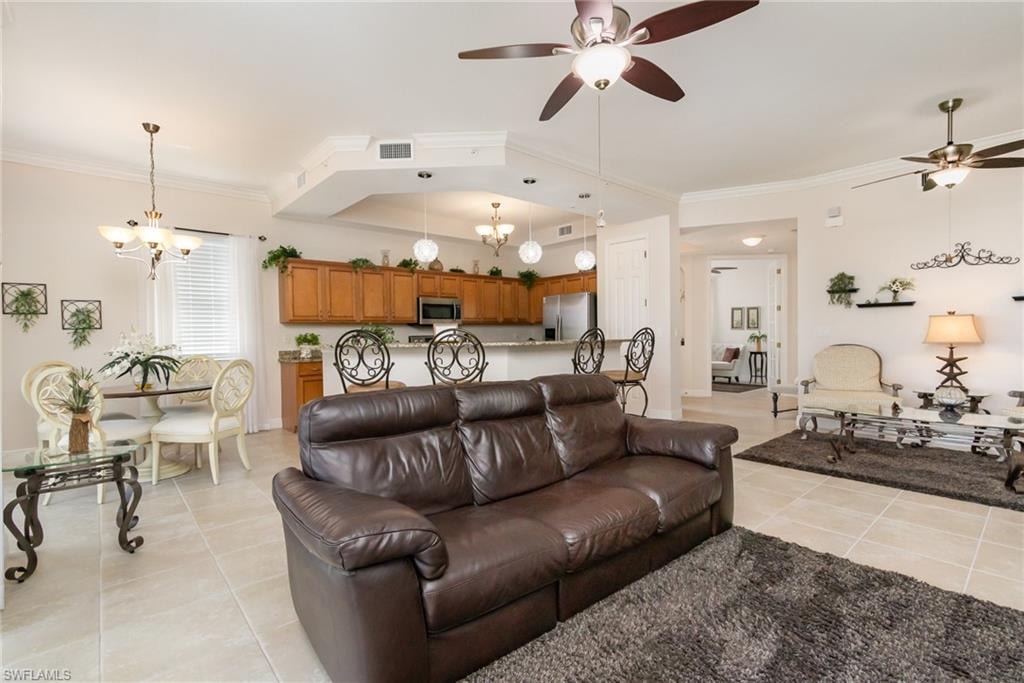 Living area with ceiling fan with notable chandelier, ornamental molding, visible vents, and light tile patterned floors