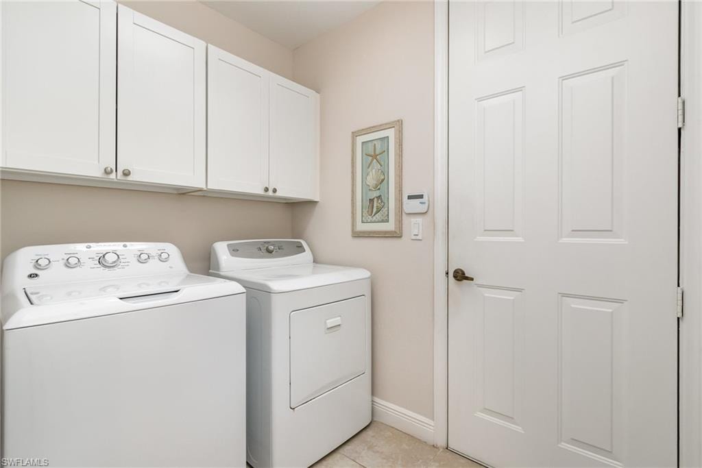 Clothes washing area with baseboards, independent washer and dryer, light tile patterned floors, and cabinet space