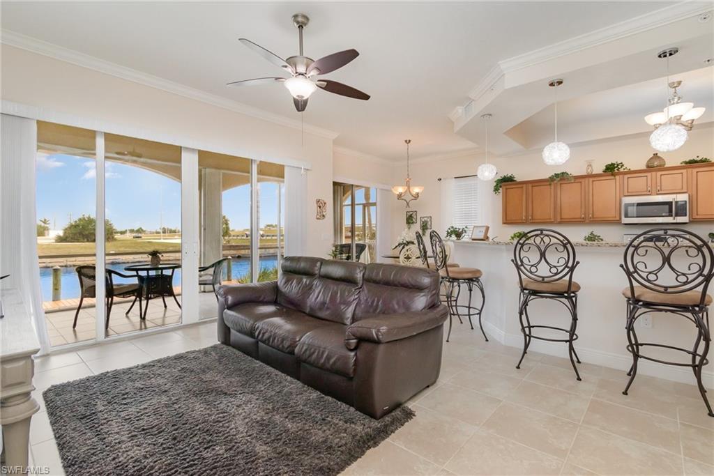 Living area with baseboards, crown molding, light tile patterned floors, and ceiling fan with notable chandelier