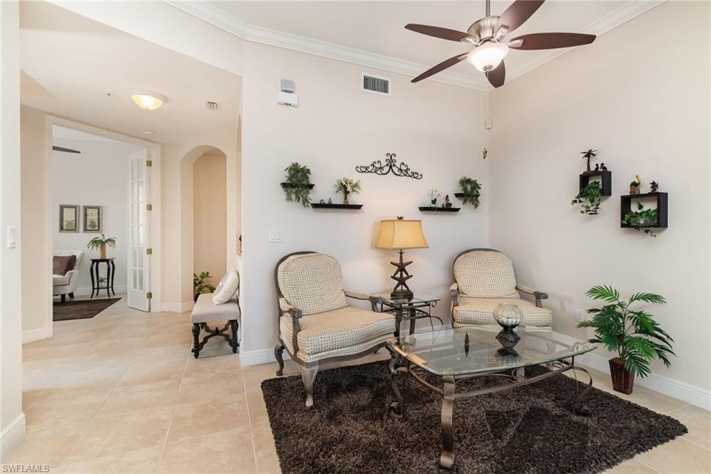 Sitting room with visible vents, light tile patterned floors, arched walkways, crown molding, and ceiling fan