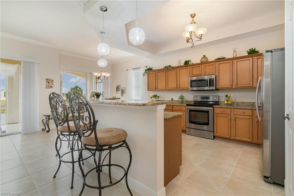 Kitchen with a breakfast bar, brown cabinetry, stainless steel appliances, and an inviting chandelier