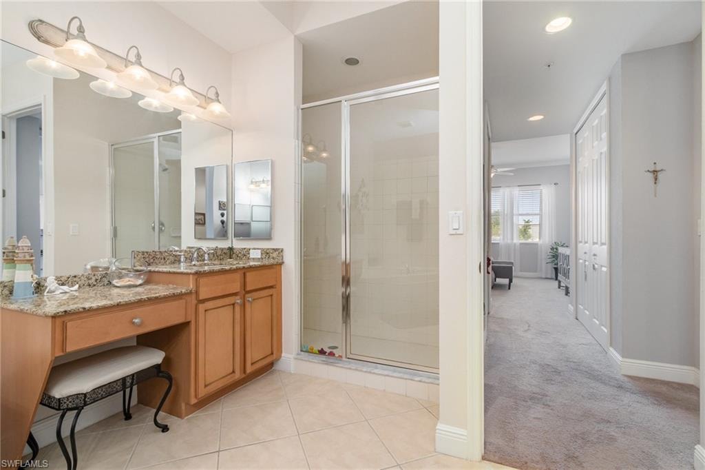 Ensuite bathroom with a shower stall, tile patterned flooring, vanity, ensuite bath, and baseboards