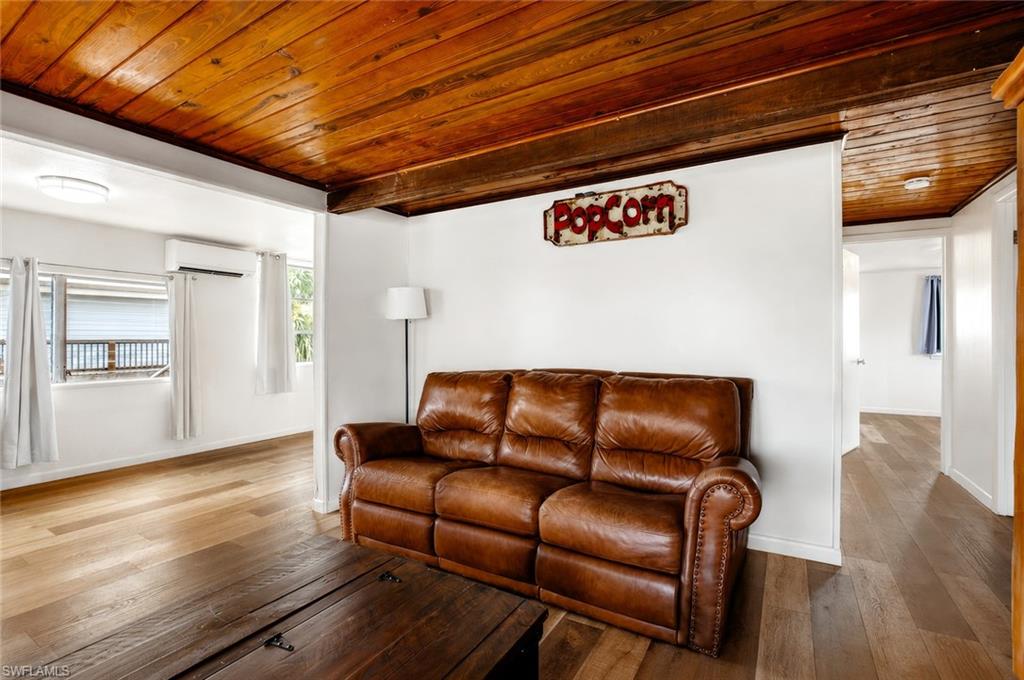 Wood-finish flooring throughout, wood-paneled ceiling, exposed wood beam, split-system air conditioning unit, and windows with roller shutters