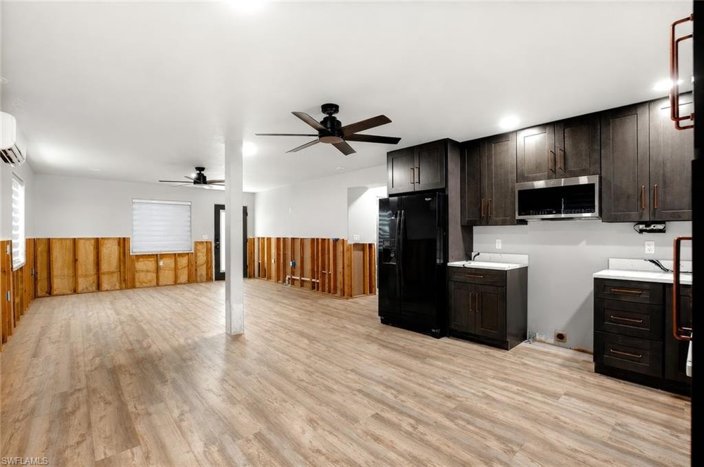 Wood-finish flooring, dark wood-finish cabinetry, stainless steel microwave, black refrigerator, and two ceiling fans