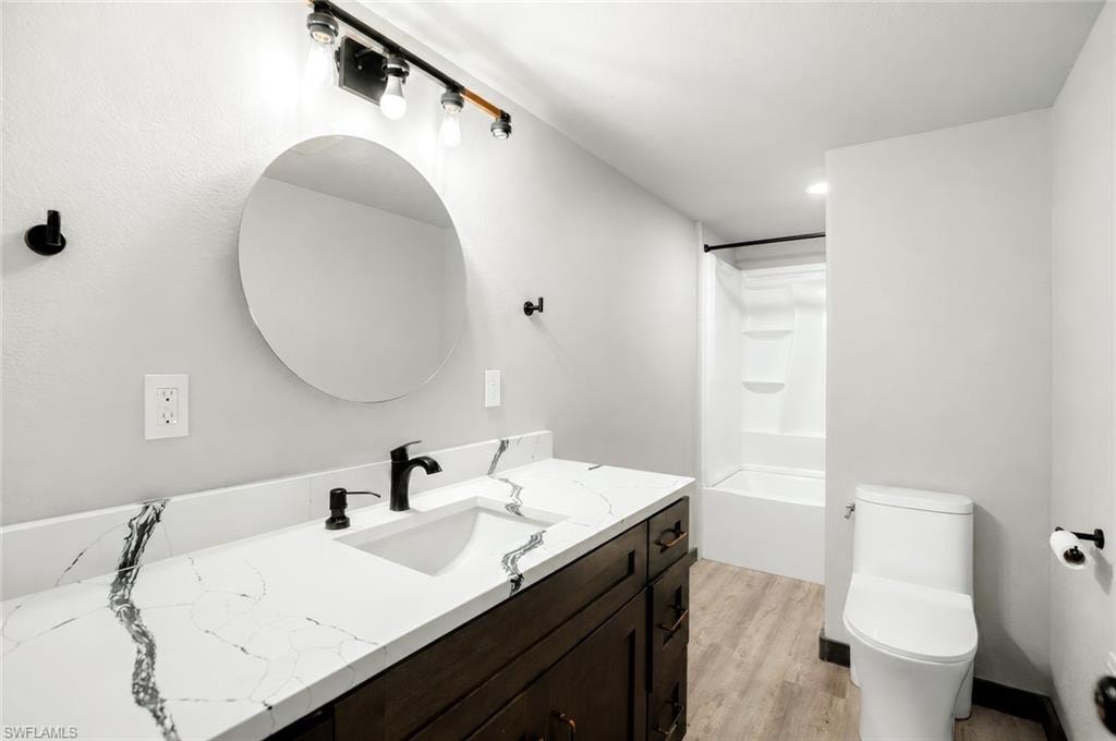 Bathroom featuring a dark wood-finish vanity, a white countertop with prominent veining, a round mirror, and a white tub with shower