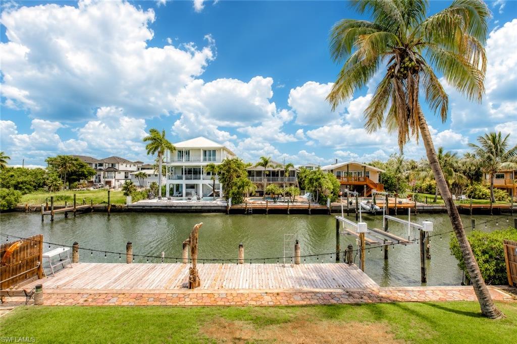 Waterfront property featuring a wood-plank dock, boat lift, manicured lawn, and mature palm trees