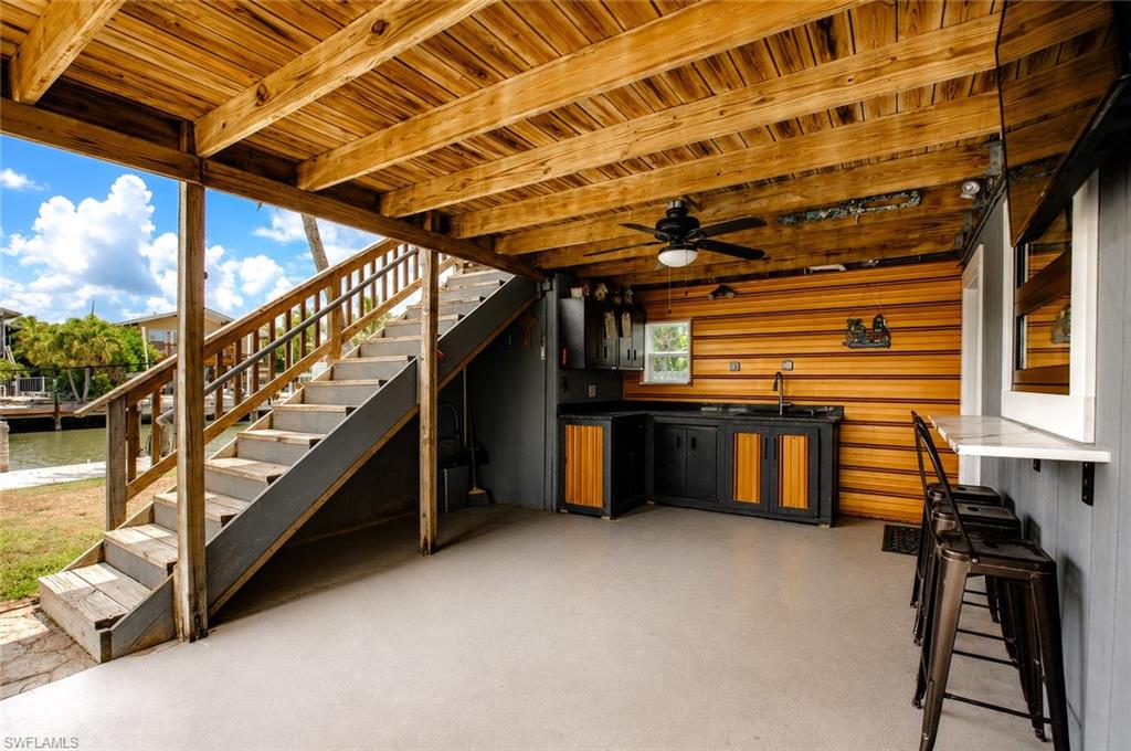 Covered outdoor space featuring a wood plank ceiling, outdoor kitchen with wood-finish cabinetry, built-in bar, and a ceiling fan
