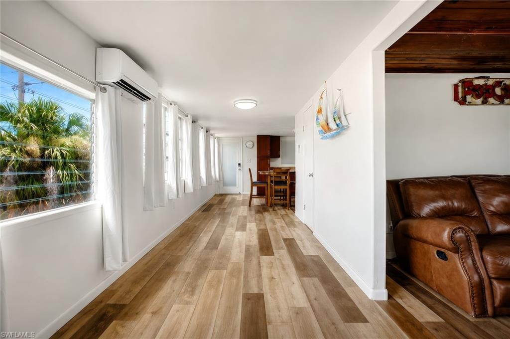 Wood-finish flooring throughout, multiple large windows, split air conditioning unit, and white interior walls