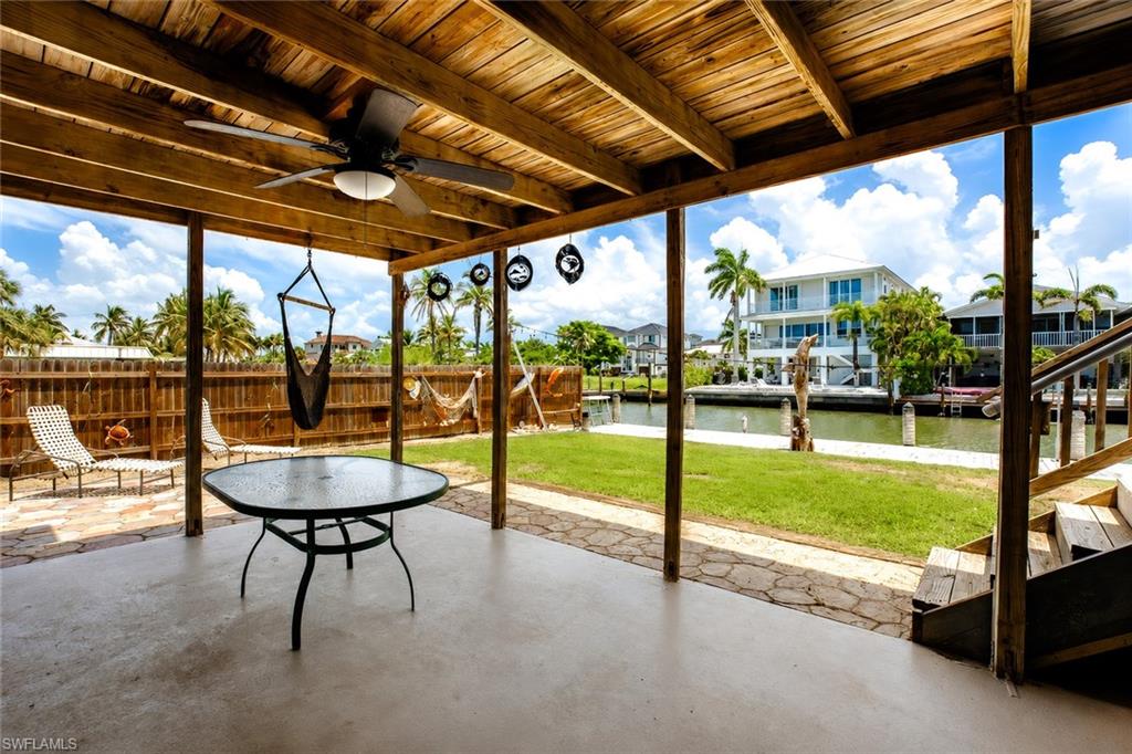 Covered patio with exposed wood beam ceiling, ceiling fan, concrete flooring, and a stone-paver border