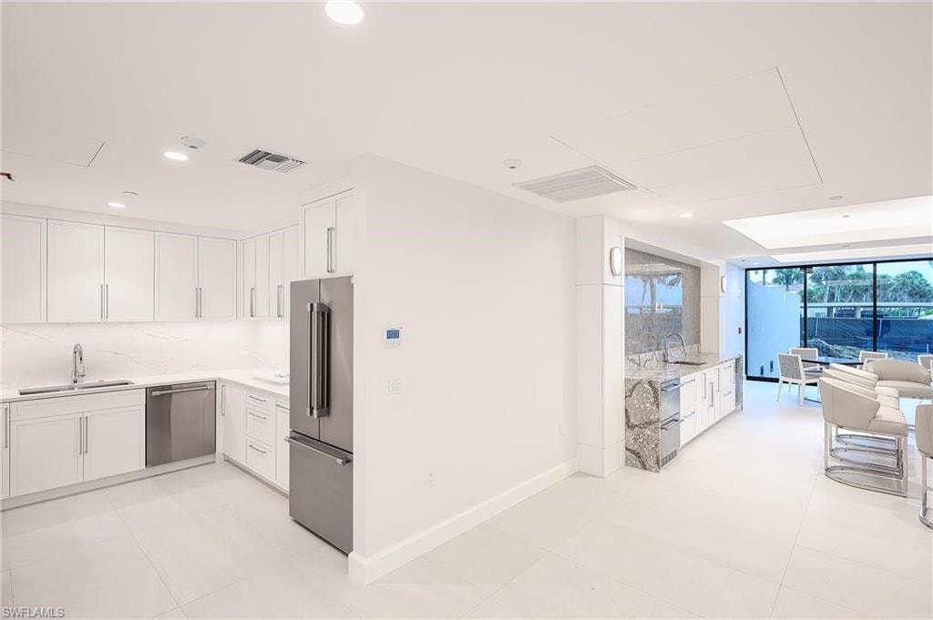 Kitchen featuring white cabinetry, light stone counters, appliances with stainless steel finishes, recessed lighting, and expansive windows