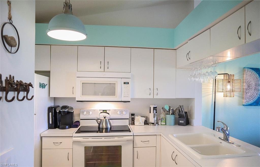 Kitchen with light countertops, a sink, white cabinetry, and white appliances