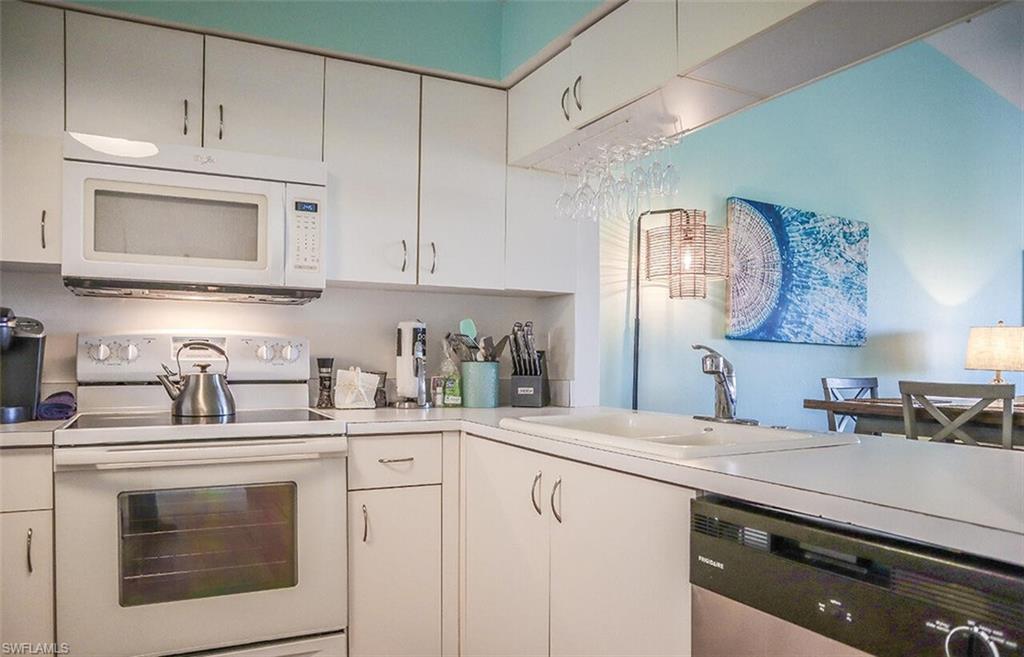 Kitchen featuring white appliances, light countertops, white cabinets, and a sink
