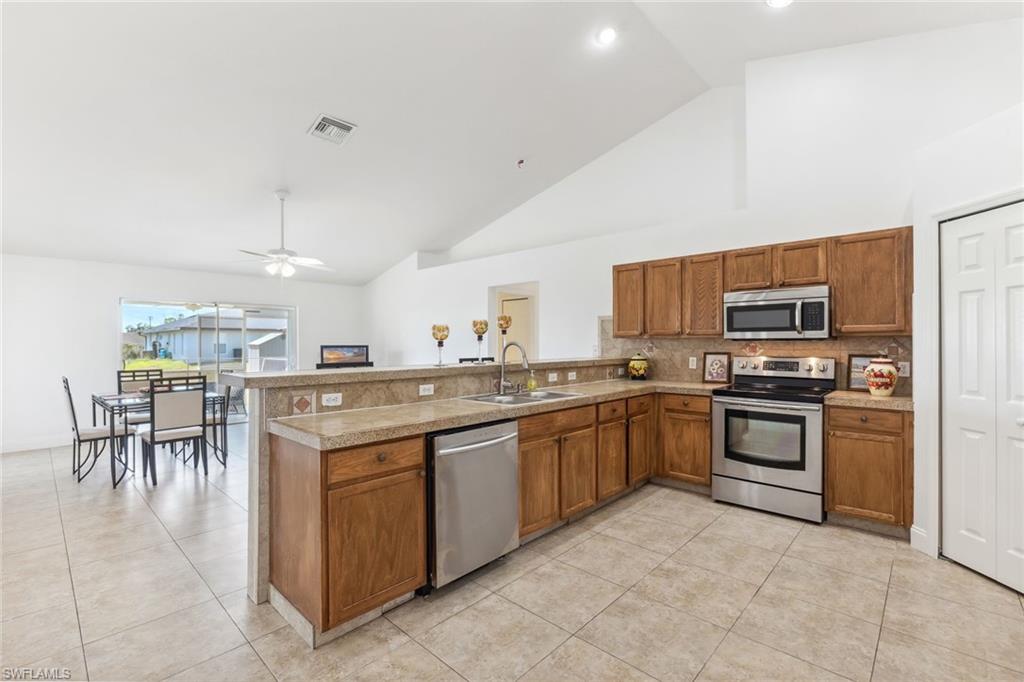 Kitchen featuring stainless steel appliances, a peninsula, a sink, visible vents, and brown cabinetry